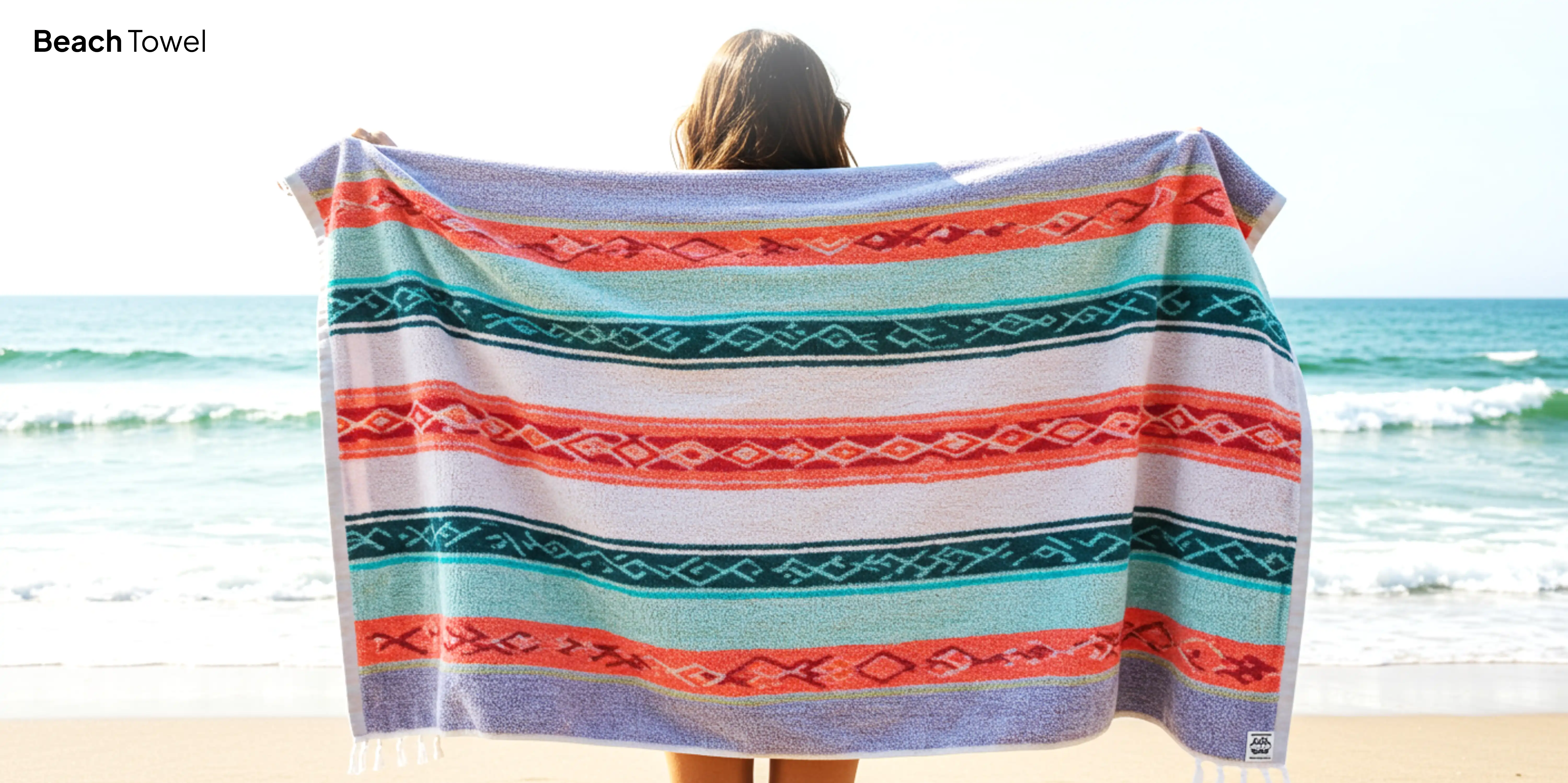 Woman holding colorful beach towel by ocean.